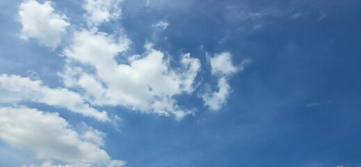 The sky is half cloudy. The clouds are on the left side of the picture while the right side is empty . The sky looks blue. The atmosphere of the sky in summer. White clouds floating all over the sky. 