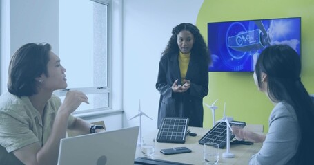 Presenting engineer in black blazer leading discussion at meeting table with wind and solar models