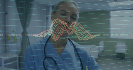 Doctor in light blue scrubs with stethoscope analyzing graphs on digital display in hospital room