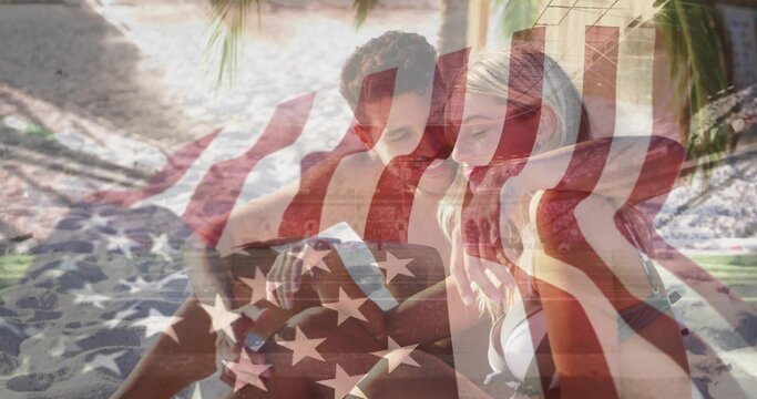 Couple examining folded map on beach mat on sand under tropical palm frond canopy, with sunglasses