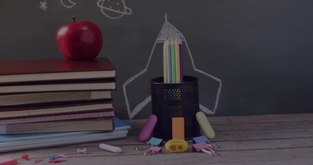 Obraz premium Holding colored pencils, pencil holder sitting in class with apple-topped textbooks and chalkboard