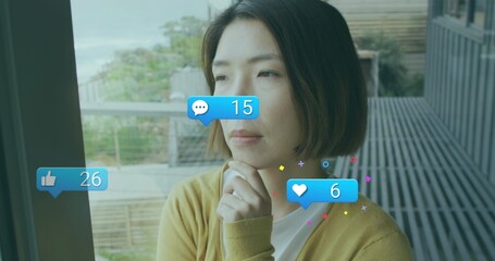 Gazing woman wearing mustard cardigan leaning on glass door on balcony, with floating social icons