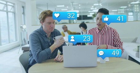 Reviewing two colleagues sitting at round table in lounge, with laptop coffee social media icons