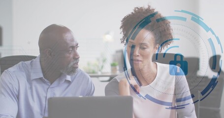 Colleagues reviewing cybersecurity interface at desk in office, with digital lock overlay on laptop