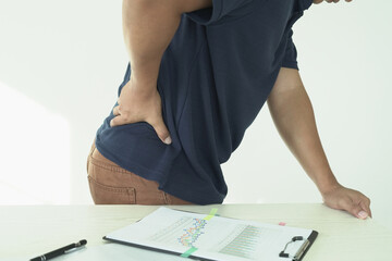 An asian businessman overworks and feels pain in his back from using a laptop, hand holding and rubbing hurt area, numbness in the waist area and back and a kind of health care and medical concept.	
