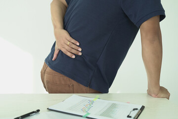 An asian businessman overworks and feels pain in his back from using a laptop, hand holding and rubbing hurt area, numbness in the waist area and back and a kind of health care and medical concept.	
