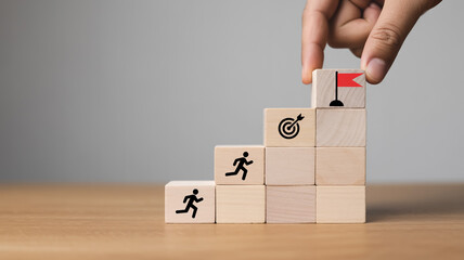 Minimalist photograph of stacked beige wooden blocks with icons, finger touching top block, symbolizing personal growth, career success, ambition, and achievement, soft side lighting.