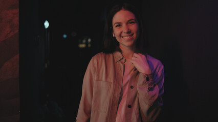 Smiling young woman poses with confidence in a dimly lit venue, showcasing her casual style during a lively night out with friends