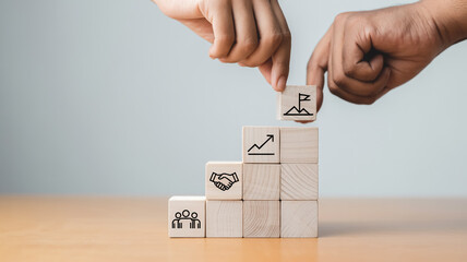 Minimalist business concept with wooden blocks forming stairs, two hands placing final cube, symbolizing teamwork, growth, unity, leadership, success, and partnership on bright table.