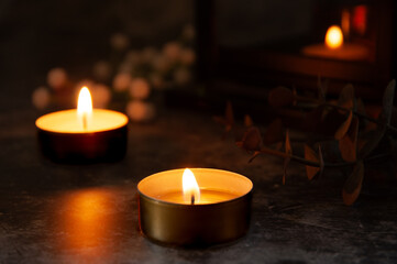 Close-up of two tealight candles glowing softly in the dark with blurred lights in the background....