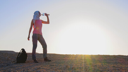 Traveler in Egypt drinking water in the desert at sunset, enjoying a moment of rest and adventure during a memorable vacation.