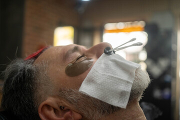 Unrecognizable master barber removes hair from nose of man with wax