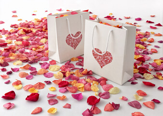 Gift bags with rose petals and hearts on a white background