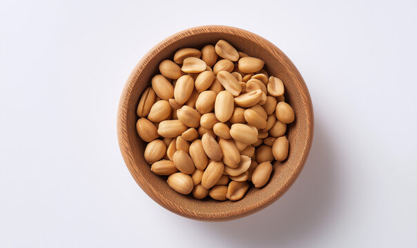 An overhead, close-up shot of a small wooden bowl filled with shelled, roasted peanuts (groundnuts), isolated on a white background.