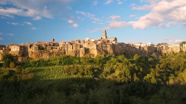 Medieval hill town of Pitigliano in Tuscany Italy built on volcanic tuff cliff glowing under warm sunlight surrounded by lush green valley and blue sky symbolizing resilience and heritage.