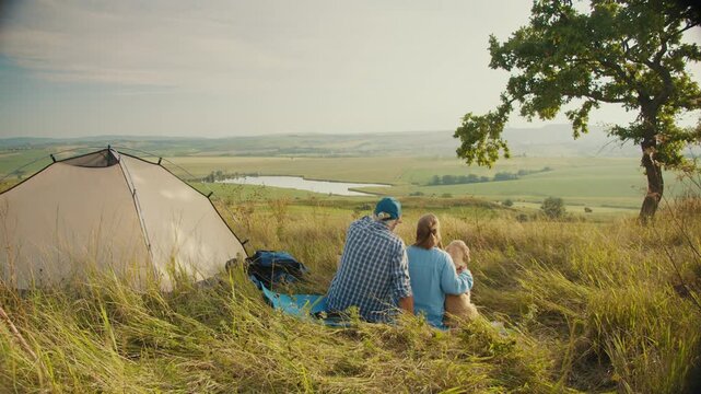 Pet-Inclusive Family Time. Senior Man Sits With His Family and Dog by a Tent, Admiring the Beautiful Landscape. A Peaceful Moment of Togetherness, Nature, and Joyful Living With a Beloved Pet