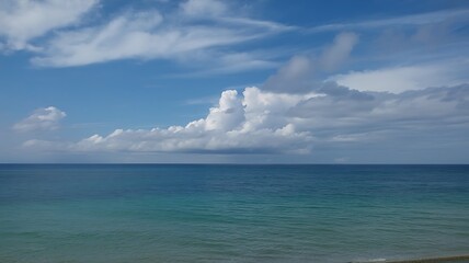 Serene coastal view showcasing the vast ocean under a vibrant blue sky with fluffy white cumulus clouds creating a breathtaking natural scene.
