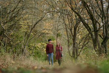 Obraz premium A candid scene of a couple walking along an autumn woodland path, capturing authenticity and warmth in their natural interaction, relaxed posture, genuine shared moment, muted tones and seasonal