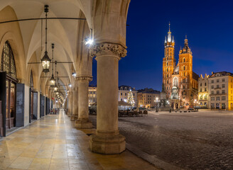 St Mary's church on snow covered Main Square in winter Krakow, Poland, illuminated in the night, with Cloth Hall arcades