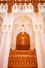 A stunning view of the grand arches, detailed ceiling, and carved wooden panels inside the Royal Opera House in Muscat, Oman. The image captures the exquisite fusion of Islamic geometric design