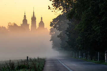 Foggy sunrise on Blonia meadow in Krakow, Poland, with St Mary's church and Town Hall towers in the background,