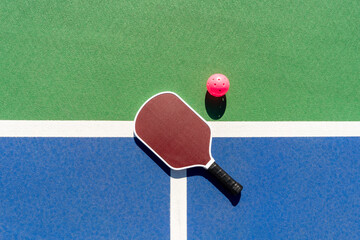 Top-down high-angle view of pickleball paddle and pink ball on green and blue outdoor court surface