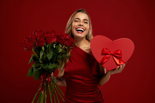 Surprised woman holding red roses and heart-shaped gift box on Valentine's Day