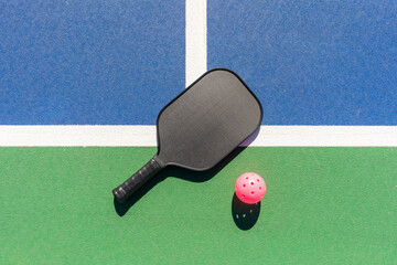 Top-down high-angle view of pickleball paddle and pink ball on green and blue outdoor court surface