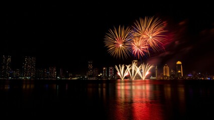 Fototapeta premium Vibrant fireworks illuminate night sky over city skyline, reflecting in calm water, perfect for celebrations and events