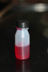 Plastic Laboratory Bottle with Red Liquid on Dark Background – Science and Chemistry Concept