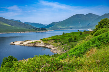 2023-06-13 A LOCH WITH A LUSH GREEN BANK AND ROLLING COUNTRYSIDE WITH MOUNTIANS IN THE BACKGROUND AND A MORNING FOG OUTSIDE OF INVERNESS SCOTLAND