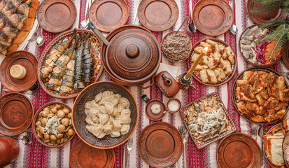 Traditional Ukrainian Christmas Eve dinner table with kutia, varenyky, stuffed cabbage rolls, fried fish, festive dishes served in bowls on embroidered rushnyk, authentic Sviat Vechir meal top view