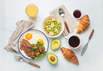 Breakfast table healthy foods fried eggs, bacon, oats fruit, avocado, croissants, coffee, orange...