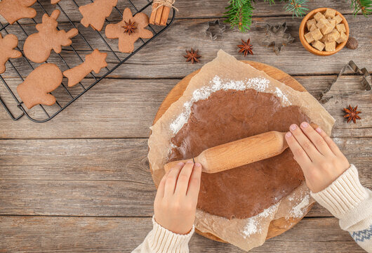 Homemade Christmas gingerbread cookies preparation, rolling dough with wooden pin on rustic table, festive baking process with cookie cutters, fir branches, and sugar cubes, top view with copy space