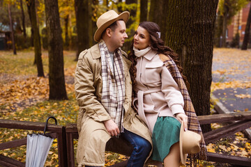 Charming couple enjoying a cozy moment outdoors in a city park during autumn. They share a joyful smile, conveying warmth and connection on a sunny day.