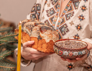 Traditional Ukrainian Christmas kutia and homemade bread in hands of woman wearing embroidered shirt, festive ritual meal of Holy Supper candle fir branches, authentic ethnic celebration scene
