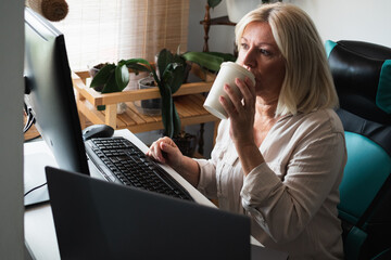 Senior woman working remote from home office drinking coffee
