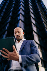 Businessman looking at tablet from below, portraying immersive concentration, digital efficiency and critical evaluation in mobile-first professional context.