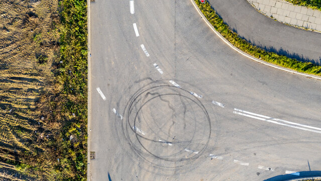 Drone view of a road intersection with visible tire marks from spinning and hard acceleration left by cars on the asphalt surface.