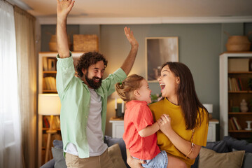 Family members share laughter and excitement at home, where they are playing together. The warm...
