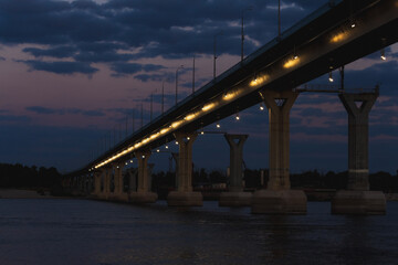 Bridge illuminated at dusk over calm water in urban setting