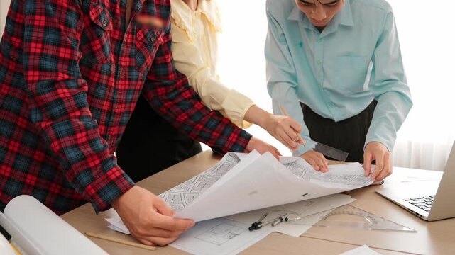Professional engineer team discussion about house design on meeting table with architectural equipment and building blueprint scatter around at modern office. Focus on hand. Closeup. Delineation.