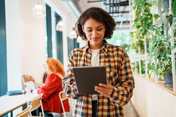 A young woman uses a tablet in a trendy cafe with vibrant decor and a lively atmosphere