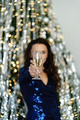 Woman in blue dress holding a glass against a background of a Christmas tree with sparkles