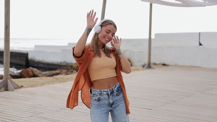 Young Caucasian woman wears orange shirt casual clothes listen to music in headphones dance rest relax in free time walk on sea ocean sand shore beach outdoor seaside in summer day. Lifestyle concept