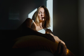 Deep portrait of thoughtful mature woman sitting in sunlight beam of dark room. Silhouette of sad...