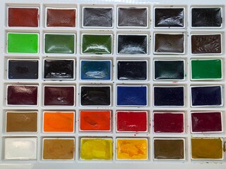 Full watercolor palette with assorted vibrant paint pans. Top-down view of a complete watercolor set featuring a variety of bright and dark colors in neatly arranged rectangular pans