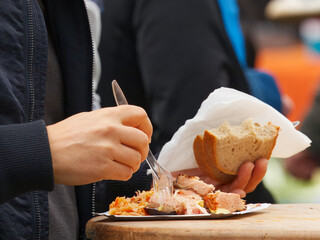 Close-up of a person eating a traditional pork dish with bread at a street food market on Náplavka in Prague. Authentic local flavors and relaxed atmosphere of outdoor dining.
