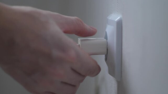 Faulty phone charger with damaged wire insulation being unplugged from socket by hand, danger from household electrical appliances