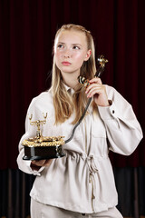 A young, beautiful woman holds an old desk telephone. Close-up against a theater curtain.
